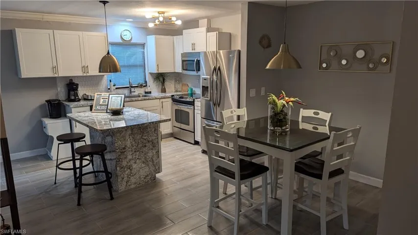Kitchen with a notable chandelier, appliances with stainless steel finishes, tasteful backsplash, a center island, and ornamental molding