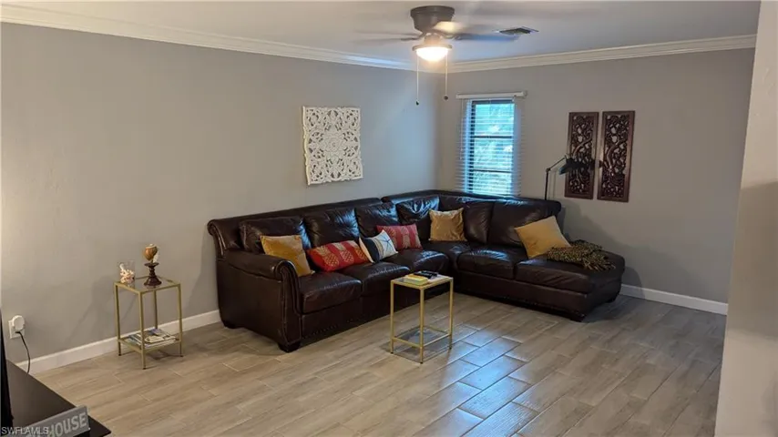 Living room featuring light wood-type flooring, ceiling fan, and crown molding