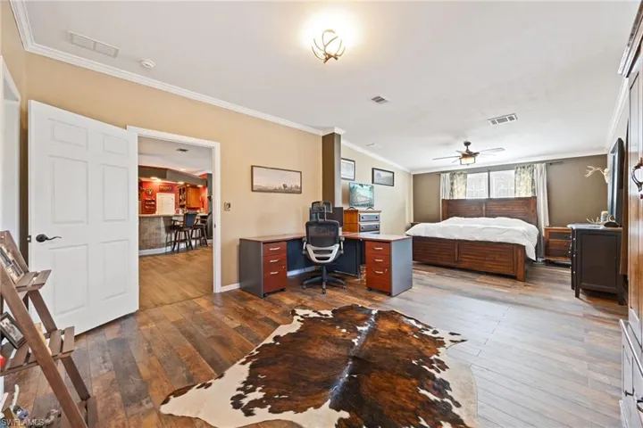 Bedroom with ornamental molding, dark wood-style floors, a ceiling fan, and an office area