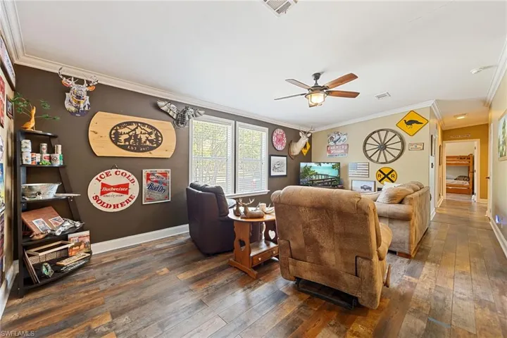 Living room featuring dark wood-style flooring, crown molding, and a ceiling fan