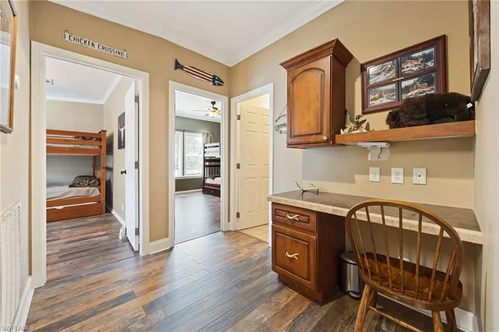 Office space featuring built in study area, ornamental molding, dark wood-style flooring, and a ceiling fan
