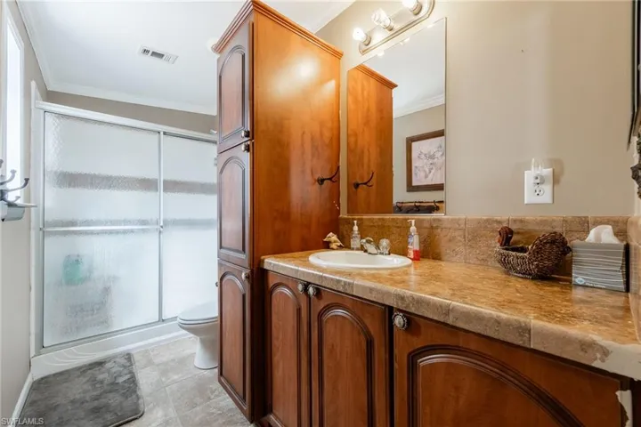 Bathroom with crown molding, vanity, a shower stall, light tile patterned flooring, and decorative backsplash