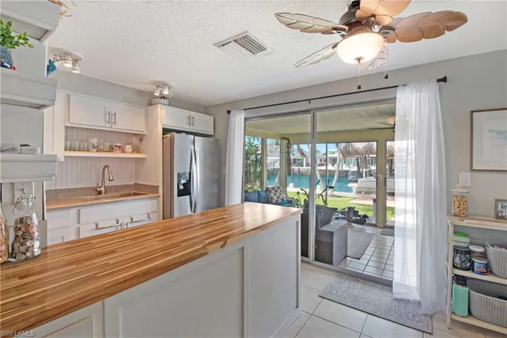 Kitchen featuring wood counters, stainless steel fridge, sink, light tile patterned floors, and white cabinetry