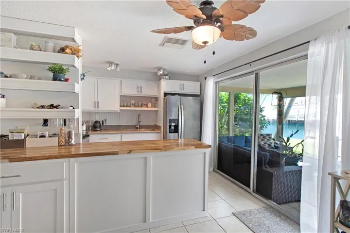 Kitchen with white cabinetry, light tile patterned floors, stainless steel fridge, and butcher block counters