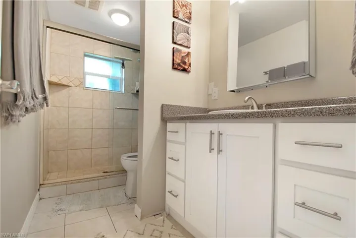Bathroom featuring tiled shower, tile patterned floors, toilet, and vanity