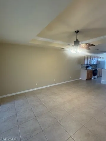 Unfurnished living room with a raised ceiling, ornamental molding, ceiling fan, and light tile patterned floors