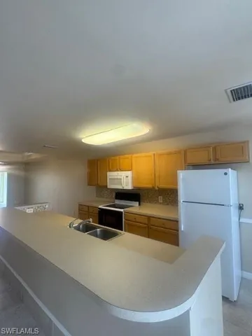 Kitchen with stove, fridge, light countertops, decorative backsplash, and light tile patterned flooring