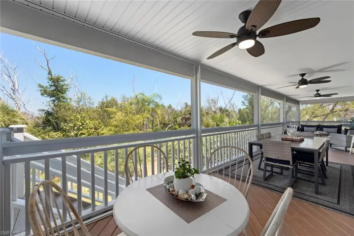 Expansive screened porch featuring wood-finish flooring, multiple ceiling fans, white railing, and a clear natural backdrop