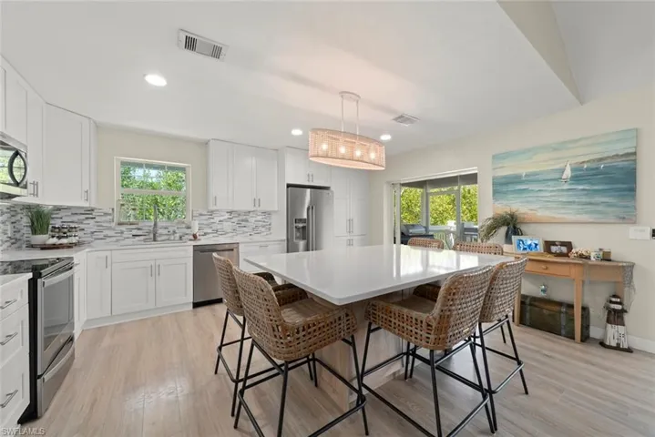 Kitchen featuring light-finish flooring, white cabinetry, a tiled backsplash, and stainless steel appliances