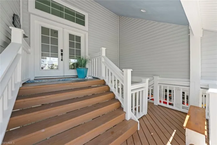 Front entry featuring double glass-panel doors with transom window, leading to a covered porch with wood-finish decking and white railings