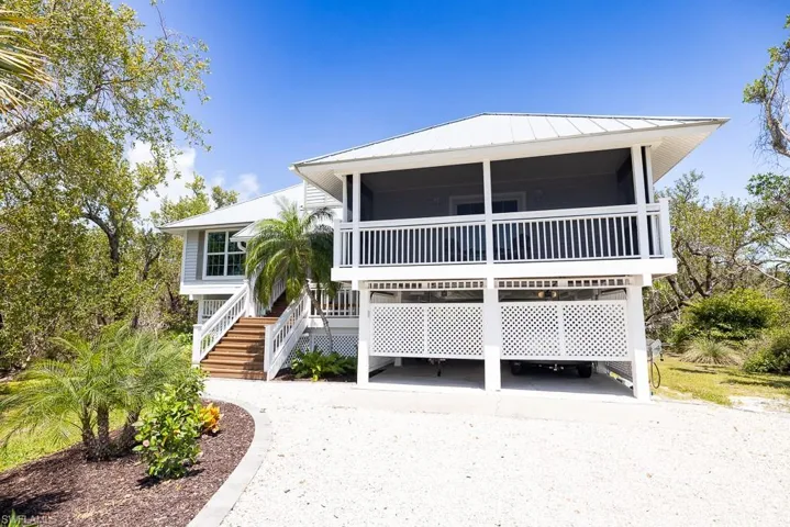 Elevated coastal residence featuring a screened-in porch, metal roof, wood-finish exterior stairs, and a white lattice enclosure for the ground-level parking area