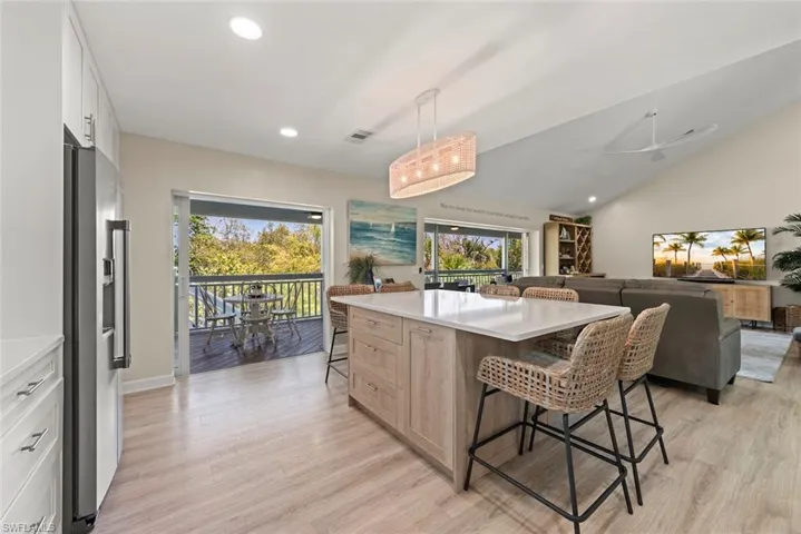Open concept living space featuring wood-finish flooring, a kitchen island with seating, white cabinetry, a stainless steel refrigerator, and a balcony with a dark railing