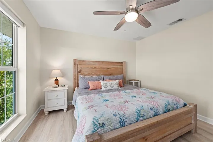 Bedroom featuring light-tone wood-finish flooring, a ceiling fan with light fixture, and a large window with white framing