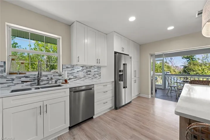 Modern kitchen featuring white shaker cabinetry, stainless steel appliances, a mosaic tile backsplash, and wood-finish flooring