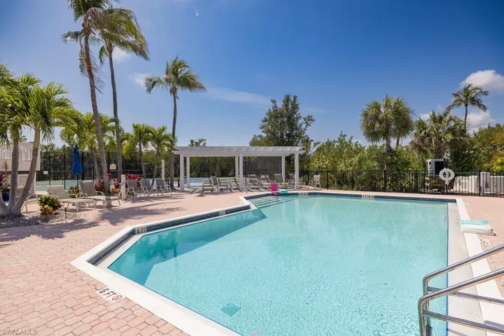 Outdoor swimming pool with brick paver decking, surrounded by palm trees and lush landscaping