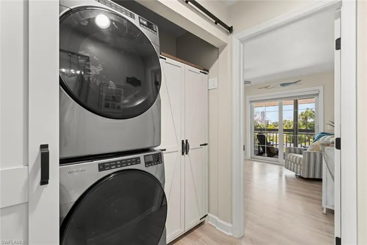 Modern stacked washer and dryer in a dedicated laundry alcove featuring white paneled barn doors and wood-finish flooring