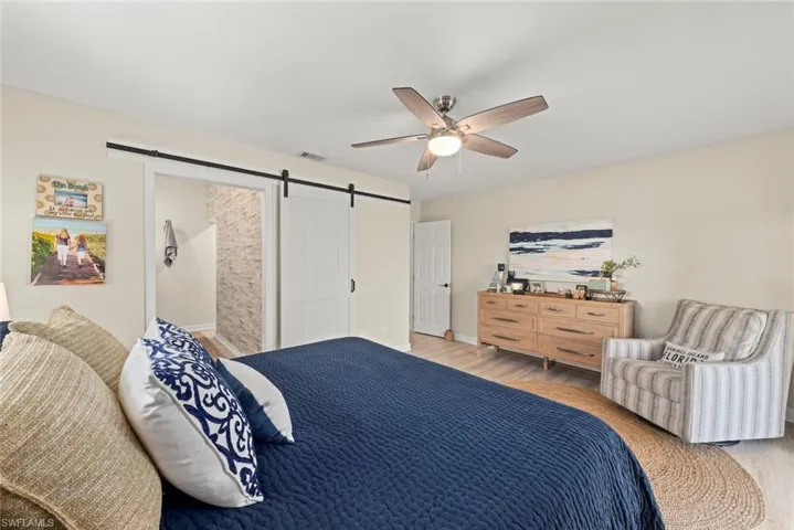 Bedroom featuring wood-finish flooring, a ceiling fan with integrated lighting, and a barn door entry to an adjoining space with a tiled wall