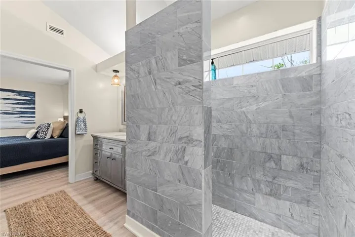 Spacious walk-in shower featuring large format gray stone tile walls and a white penny tile floor