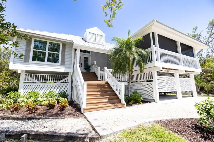Elevated coastal-style residence featuring a metal roof, screened porch, wood-finish exterior stairs, lattice foundation skirting, and gravel driveway