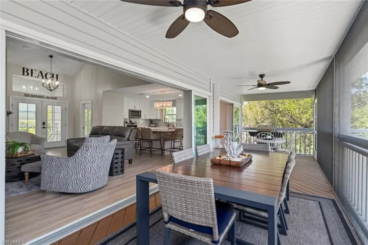 Expansive screened outdoor living area featuring dual ceiling fans, wood-finish flooring, and a privacy screen