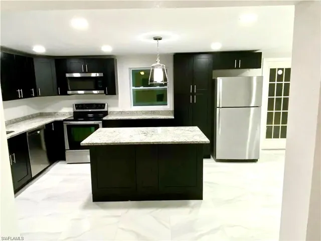 Kitchen with stainless steel appliances, dark cabinetry, a kitchen island, and light stone countertops