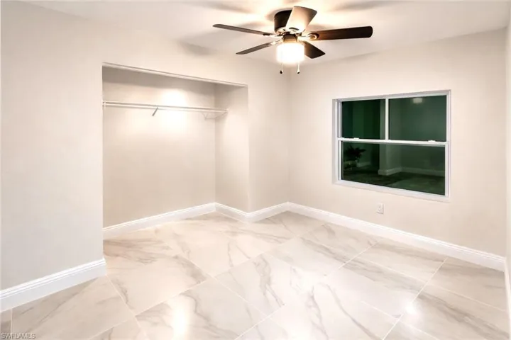 Unfurnished bedroom featuring ceiling fan, a closet, and light marble finish flooring