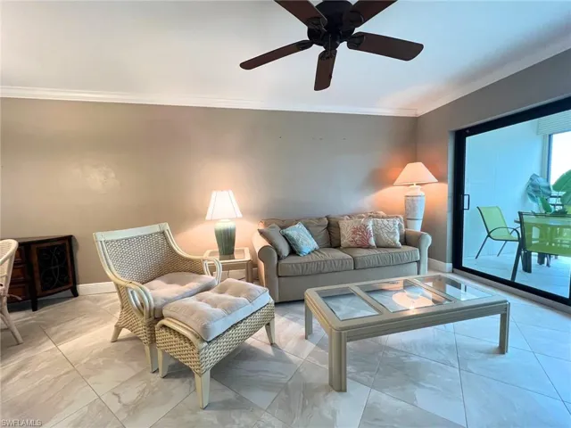 Living room with crown molding, marble look tiles, and a ceiling fan