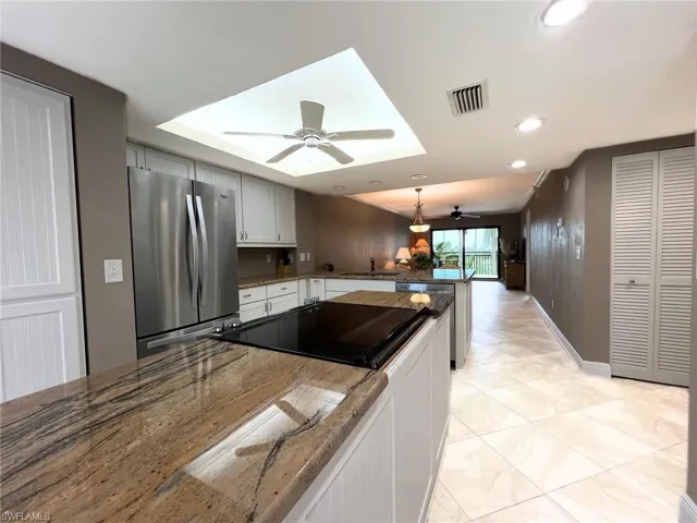 Kitchen with freestanding refrigerator, a peninsula, pendant lighting, white cabinetry, and dark stone countertops
