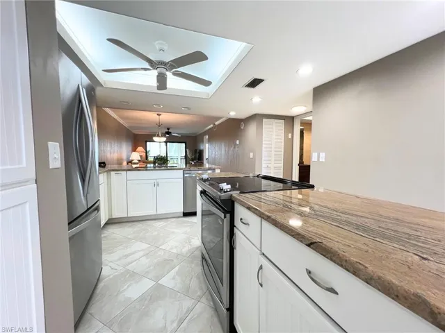 Kitchen with stainless steel appliances, white cabinetry, dark stone countertops, a peninsula, and ornamental molding