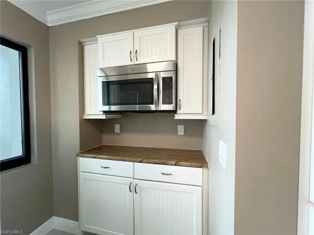 Kitchen featuring white cabinets, dark countertops, stainless steel microwave, and ornamental molding