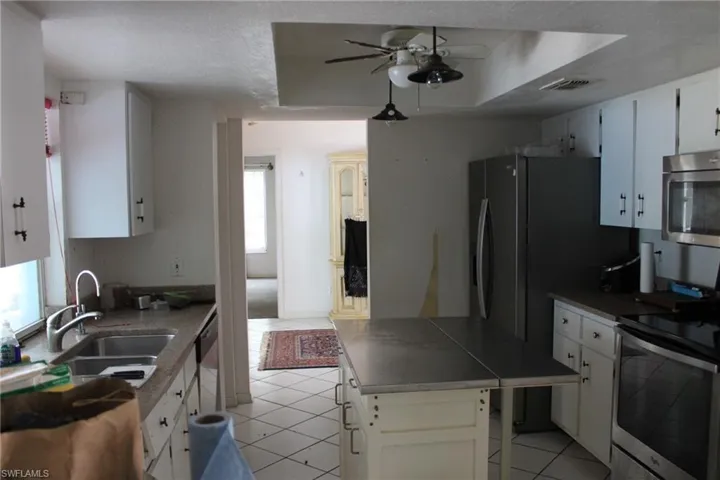 Kitchen featuring a raised ceiling, white cabinets, light tile patterned floors, and appliances with stainless steel finishes