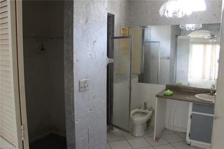 Bathroom with tile patterned floors, walk in shower, vanity, ceiling fan with notable chandelier, and a bidet