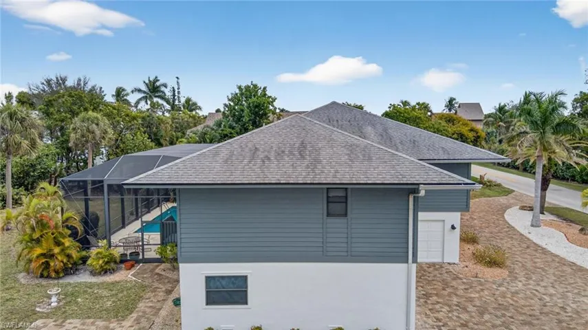 View of side of property featuring glass enclosure, a sunroom, roof with shingles, an outdoor pool, and stucco siding