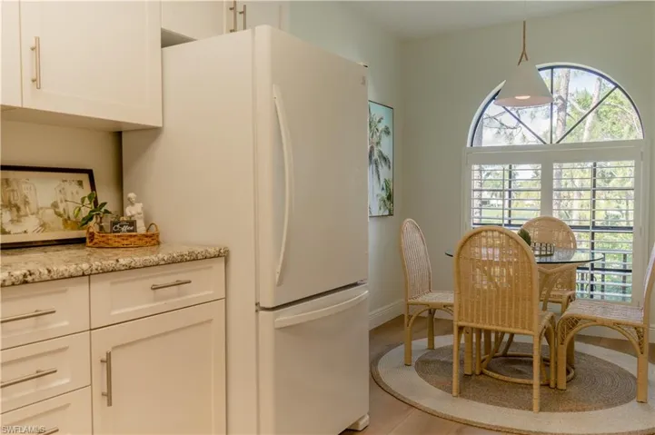 Kitchen featuring light wood-type flooring, light stone counters, freestanding refrigerator, and white cabinetry