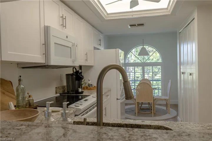 Kitchen featuring visible vents, white cabinets, a raised ceiling, white microwave, and light stone countertops