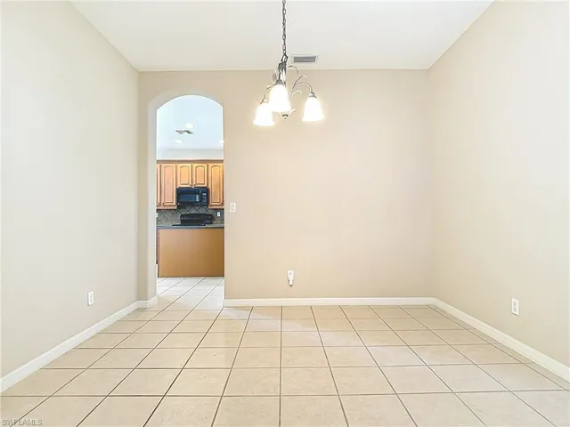 Unfurnished dining area featuring light tile patterned floors, arched walkways, and a chandelier