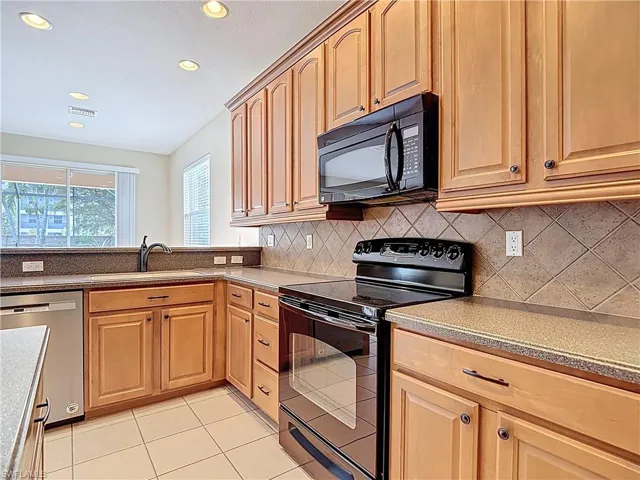 Kitchen featuring black appliances, light tile patterned floors, recessed lighting, decorative backsplash, and light stone counters