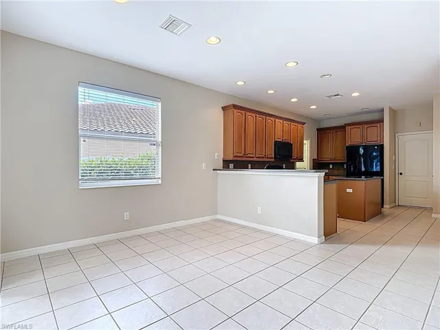 Kitchen with black appliances, brown cabinetry, light tile patterned floors, dark countertops, and recessed lighting