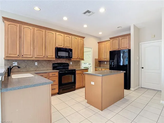 Kitchen with black appliances, a center island, tasteful backsplash, washer and clothes dryer, and light tile patterned floors