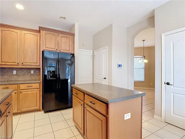 Kitchen featuring black fridge with ice dispenser, tasteful backsplash, arched walkways, light tile patterned floors, and a kitchen island