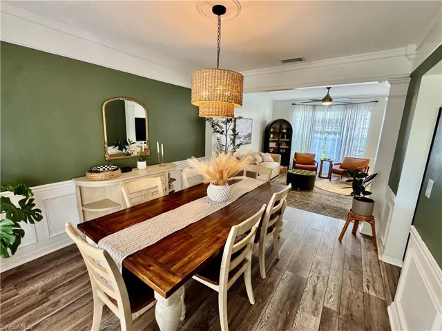 Dining room with a decorative wall, crown molding, dark wood finished floors, a chandelier, and wainscoting