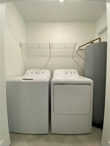 Laundry room featuring separate washer and dryer, water heater, and light tile patterned floors