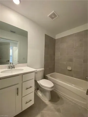 Full bathroom with tiled shower / bath combo, vanity, toilet, and tile patterned floors