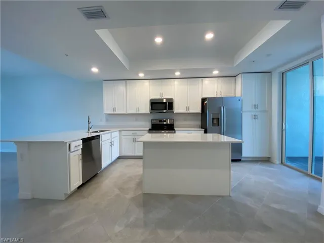Kitchen with white cabinets, a raised ceiling, a kitchen island, stainless steel appliances, and sink