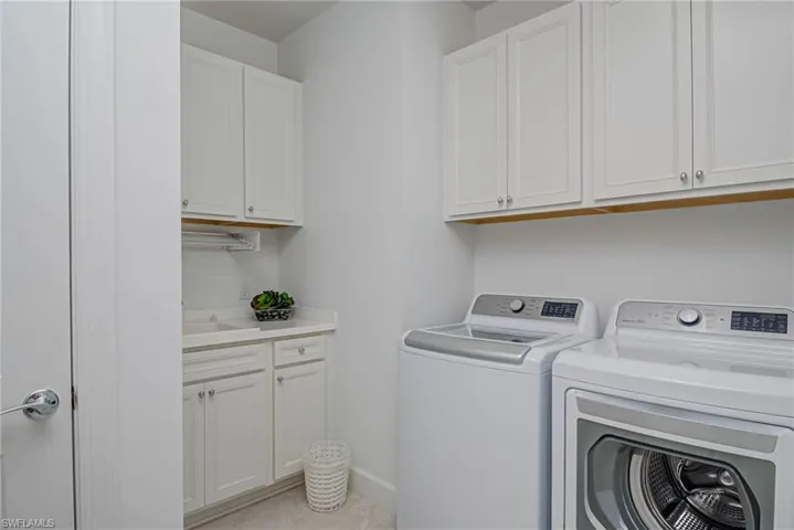 Laundry room with washing machine and dryer, cabinets, light tile patterned floors, and sink