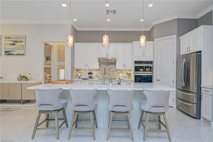 Kitchen featuring stainless steel appliances, white cabinets, a center island with sink, and hanging light fixtures