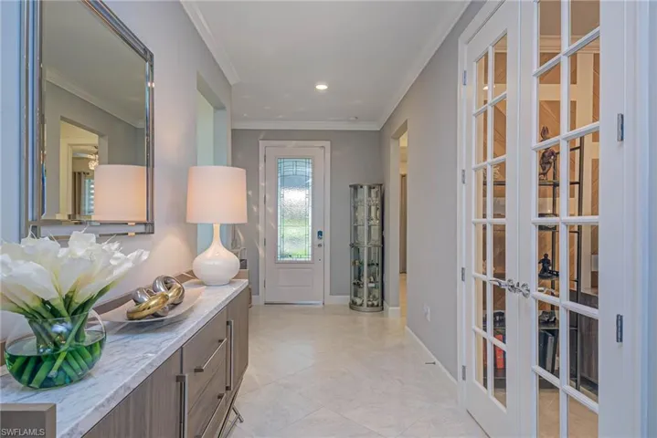 Foyer entrance with French doors, crown molding, and white brick accent wall