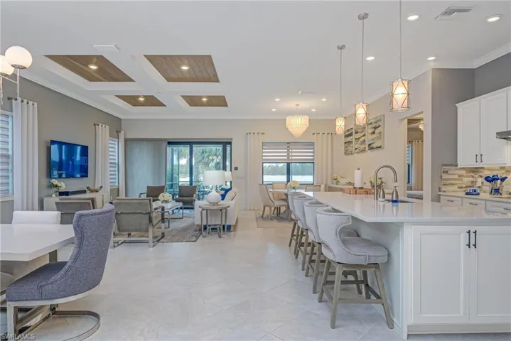 Kitchen with a center island with sink, pendant lighting, sink, coffered ceiling, and white cabinetry
