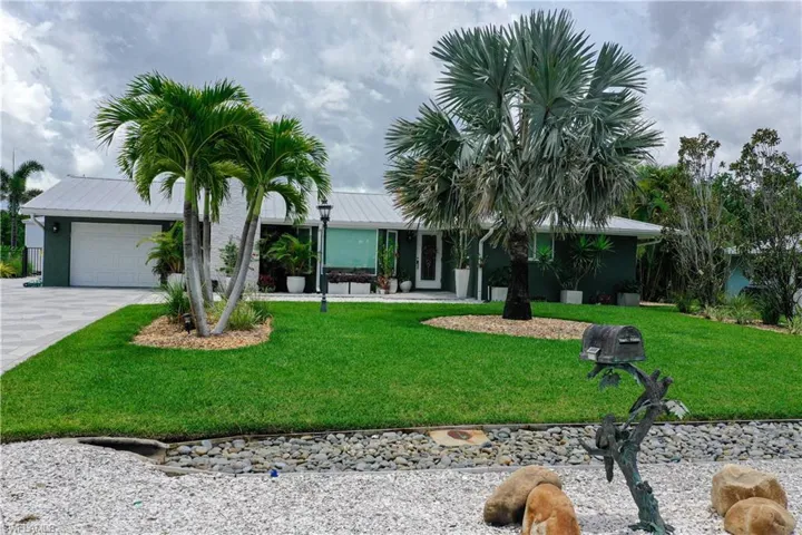 Ranch-style house with a front yard, a garage, driveway, a metal roof, and stucco siding