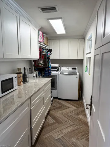 Laundry area with cabinet space, parquet flooring, independent washer and dryer, and crown molding
